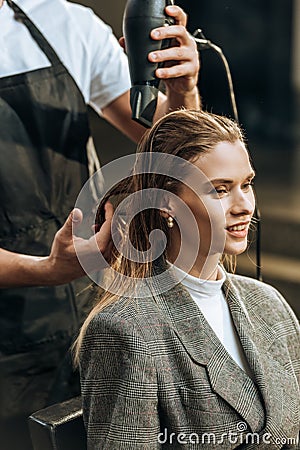 Cropped shot of hairstylist drying hair to beautiful smiling girl Stock Photo
