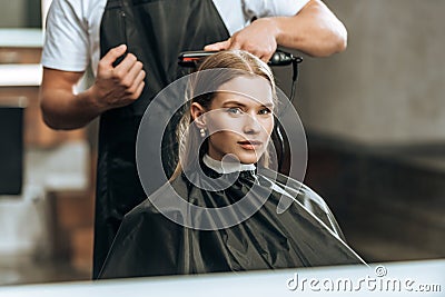 Cropped shot of hairstylist using hair straightener and girl looking at mirror Stock Photo