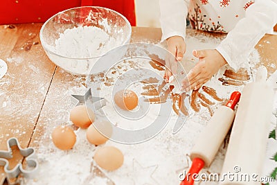 Cropped shot of little child in apron bakes something delicious on kitchen, makes cakes with hands, surrounded with Stock Photo