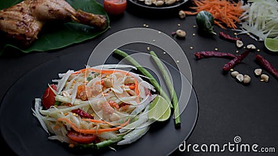 Cropped shot of papaya salad on black plate, chicken grill on green taro and ingredients Stock Photo