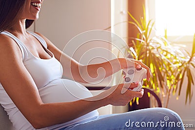 Pregnant woman holding joystick and playing video games Stock Photo