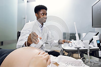 Cropped shot of a pregnant woman during ultrasound scanning, visiting her male African doctor obstetrician, using modern Stock Photo