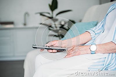 cropped shot of senior woman with remote control watching tv on sofa at home Stock Photo