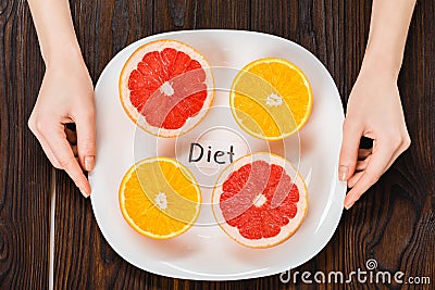 cropped shot of woman holding plate with halved citrus fruits and diet inscription Stock Photo