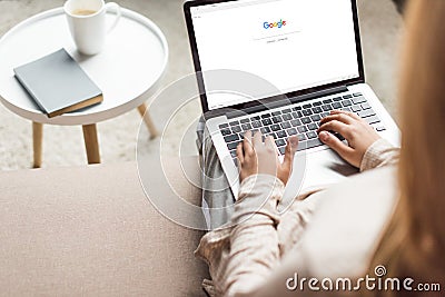 cropped shot of woman at home sitting on couch and using laptop with google website Editorial Stock Photo