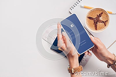 cropped shot of woman with smartphone with facebook logo on screen at tabletop with cup of coffee ticket Editorial Stock Photo