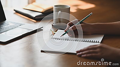 Cropped shot of writer woman writing her new fiction on notebook in front computer laptop at the modern wooden table. Stock Photo