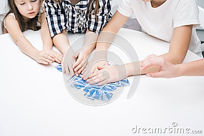 Cropped unrecognizable children hands hold blue playing cards on white table. Smart game for time, who first. Family fun Stock Photo