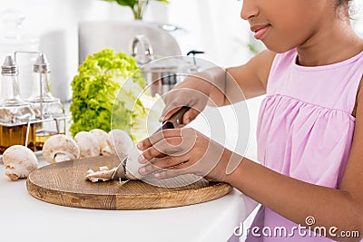 cropped view of african american kid cutting mushrooms on wooden board Stock Photo