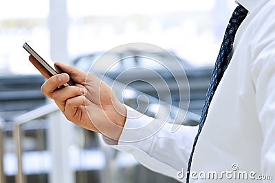 Cropped view of Businessman holding the mobile phone standing in front the window Stock Photo