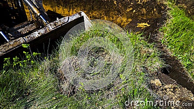 Cropped view of excavator bucket digging into grassy field during earth works Stock Photo