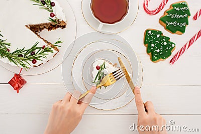 Cropped view of girl eating christmas cake and cookies on white wooden table. Stock Photo