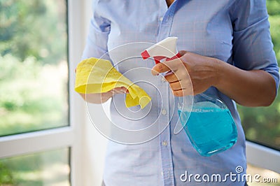 Close-up of a housewife spraying detergent on a yellow cloth while washing windows in veranda. Spring cleaning concept Stock Photo