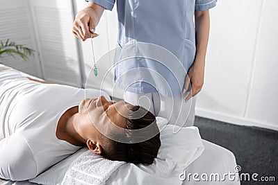 View of hypnotist standing near man on massage table and holding green stone Stock Photo