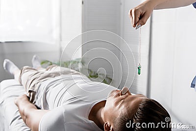 View of hypnotist standing near man on massage table and holding green stone Stock Photo