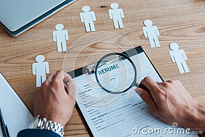 View of man holding magnifier near clipboard with resume Stock Photo