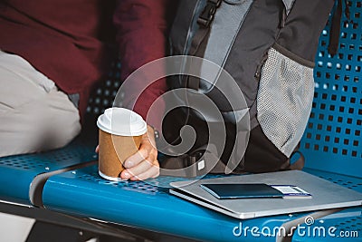 Cropped view of man holding paper cup near backpack laptop and passport Stock Photo