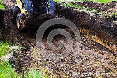 Cropped view of mini loader in foundation pit with ground in its bucket Stock Photo