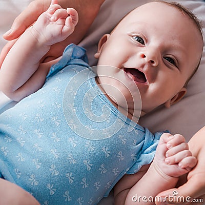View of mother holding hands of happy infant in blue baby bodysuit Stock Photo