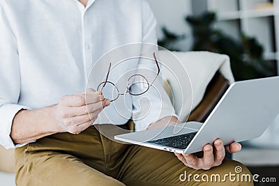 Cropped view of pensioner holding glasses and using laptop Stock Photo