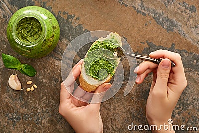 Cropped view of woman adding pesto sauce with spoon on baguette slice on stone surface Stock Photo