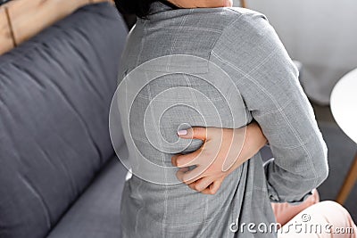View of woman with allergy scratching back while sitting on sofa Stock Photo
