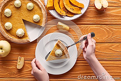 Cropped view of woman holding spatula with piece of pumpkin pie with whipped cream near baked pumpkin, cut and whole Stock Photo