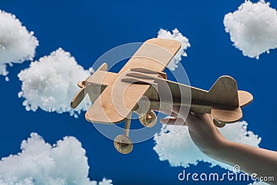Cropped view of woman holding wooden toy plane near white fluffy clouds made of cotton wool isolated on blue Stock Photo