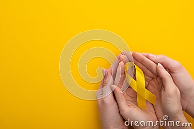 Cropped view of woman and man holding yellow ribbon on colorful background, international childhood cancer day concept. Stock Photo