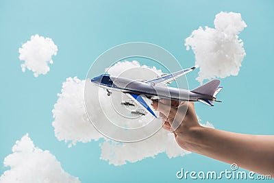 Cropped view of woman playing with toy plane among white fluffy clouds made of cotton wool isolated on blue Stock Photo