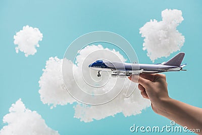 Cropped view of woman playing with toy plane among white fluffy clouds made of cotton wool isolated on blue Stock Photo