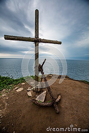 Cross and anchor on the mountain on the background of sea and sky Stock Photo