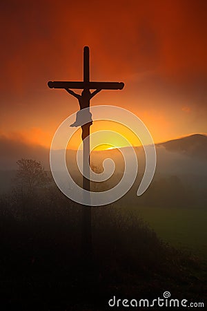 Cross with beautiful sunset with fog. Czech landscape with cross with orange sun and clouds during morning. Hilly mystic landscape Stock Photo