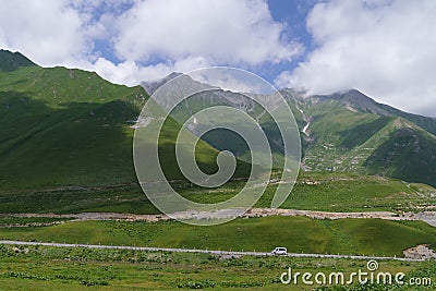 Cross pass on Georgian military road in summer and giant mountains covered with alpine meadows Stock Photo