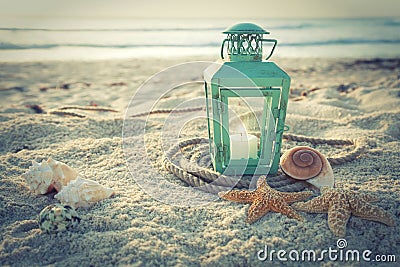 Cross-processed lantern on beach with shells and rope at sunrise Stock Photo