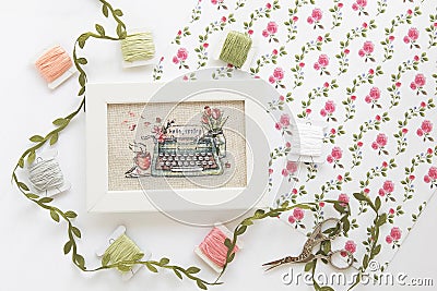 Cross stitch typewriter saying hello spring on linen canvas in white frame, floss threads on bobbins, needlework scissors, floral Stock Photo