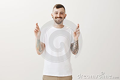 Crossing fingers for luck. Portrait of happy joyful european man with tattoos, wishing or hoping for success of business Stock Photo