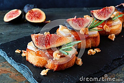 Crostini appetizers with figs, brie cheese and walnuts, close up on a slate serving board Stock Photo