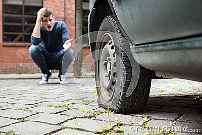 Crouched Man Pointing At Punctured Car Tire Stock Photo