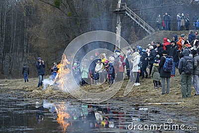 Crowd of people celebrating Masnytsya - pagan holiday of farewell to winter, burning the straw scarecrow on a riverside Editorial Stock Photo