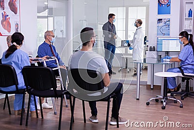 Crowded new normal hospital waiting room with patients sitting on chairs Stock Photo