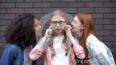 Cruel teenagers teasing female pupil eyeglasses, bullying victim covering ears Stock Photo