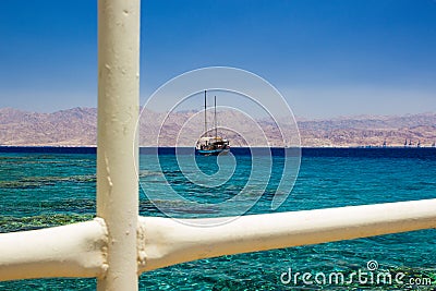 Cruise ship floating on Red sea aquamarine transparent water with coral riffs view on bottom through white fence pipes frame, Stock Photo