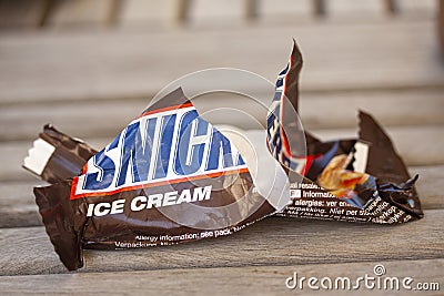 Crumbled and torn paper from a Snickers Ice Cream bar thrown on wooden floor. Close up Editorial Stock Photo