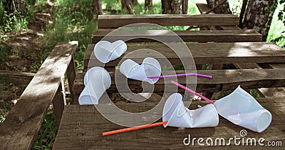 Crumpled white plastic glasses and plastic straws on a wooden table in the forest Stock Photo