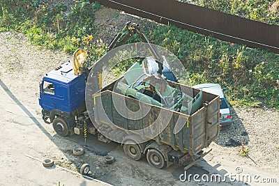 Crushed car being picked up by a grabber. An accident car has been loaded onto a dumptruck by crane. loader crane machine loading Stock Photo