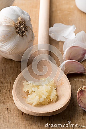 Crushed Garlic on Wooden Spoon Beside Unpeeled Cloves Stock Photo
