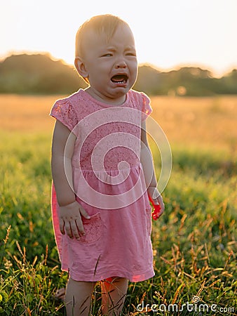 Crying baby in pink dress. Child girl in outdoor with sunset tones Stock Photo