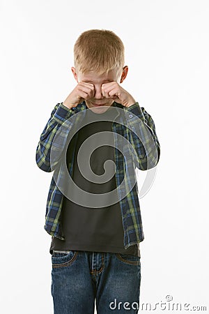 Crying boy rubs his eyes with his fists Stock Photo