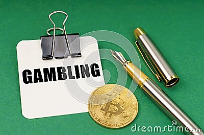 On a green surface, a bitcoin coin, a pen and a sheet of paper with the inscription - Gambling Stock Photo